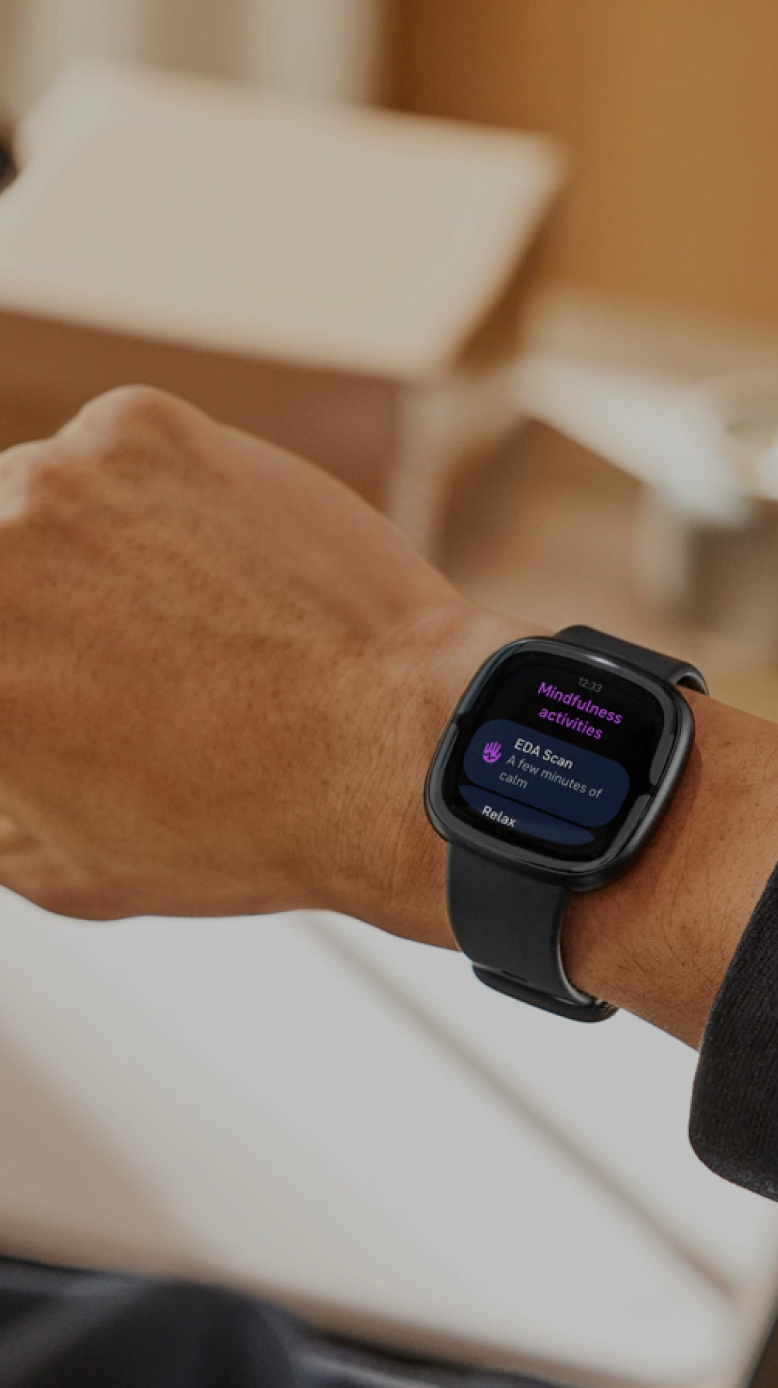 Close-up of a man’s arm wearing a Fitbit smartwatch. A Stella overlay recommends boosting hydration after recovery drops.