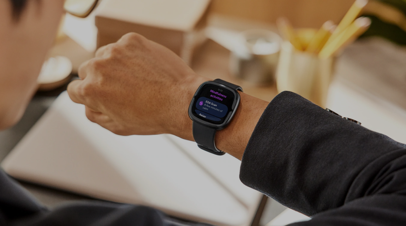 Close-up of a man’s arm wearing a Fitbit smartwatch. A Stella overlay recommends boosting hydration after recovery drops.